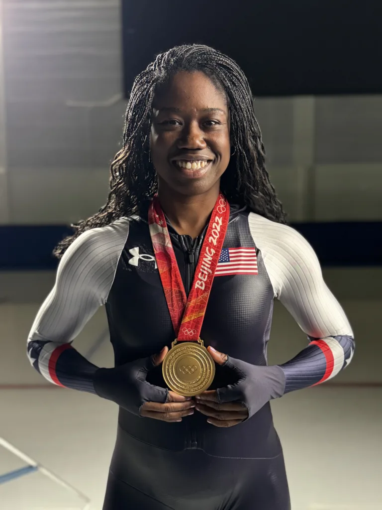 Erin Jackson holds her gold medal while wearing her Team USA racing suit.
